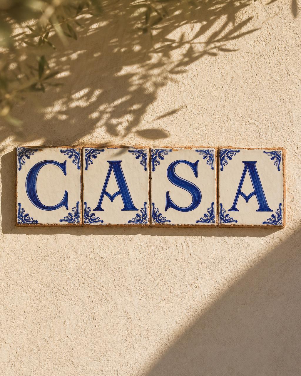 四块手绘钴蓝瓷砖拼出 CASA，嵌于阳光地中海灰泥墙
