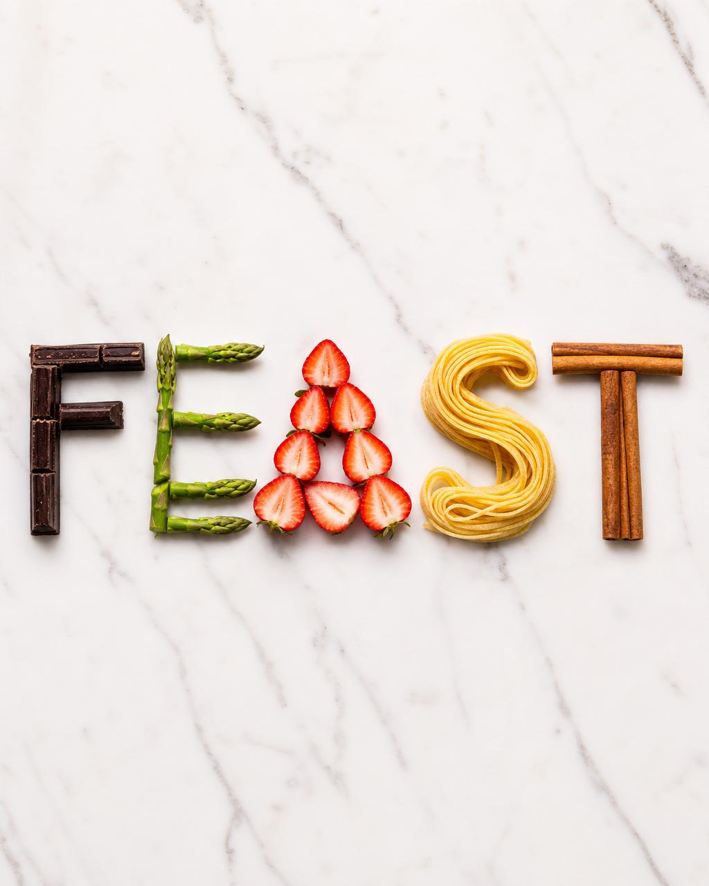 单词 FEAST 由五种食材在白色大理石上拼成——巧克力、芦笋、草莓、意面与肉桂棒各成一字