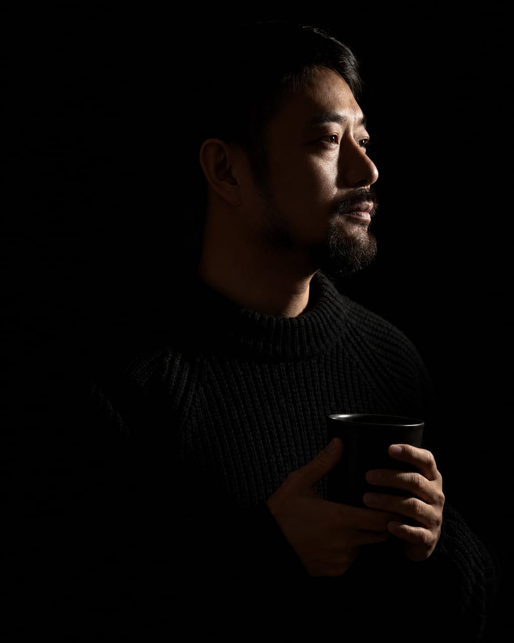 低调光胡须男性肖像：一位留短胡须的中年男性穿深灰高领，面部转向镜头左侧三十度，深炭灰无缝背景，画面只保留头肩，不需要任何道具。