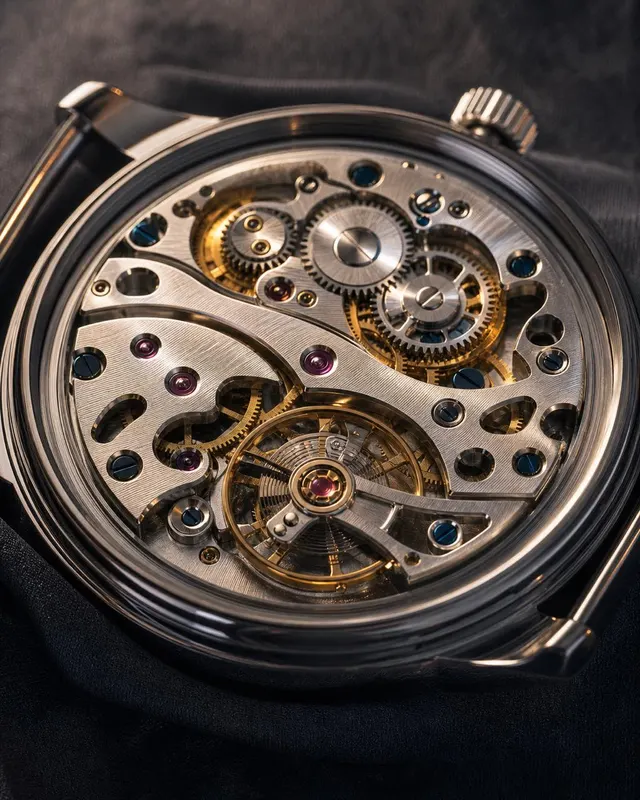 Monochrome macro of a mechanical watch showing dial and open caseback movement with escapement wheel in sharp focus on black velvet.